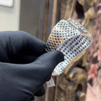 A close-up image of a hand holding a luxurious gold diamond bracelet with a sparkling blue stone, showing an openable design.