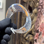 A close-up image of a hand holding a luxurious gold diamond bracelet with a sparkling blue stone, showing an openable design.