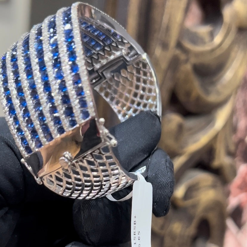 A close-up image of a hand holding a luxurious gold diamond bracelet with a sparkling blue stone, showing an openable design.