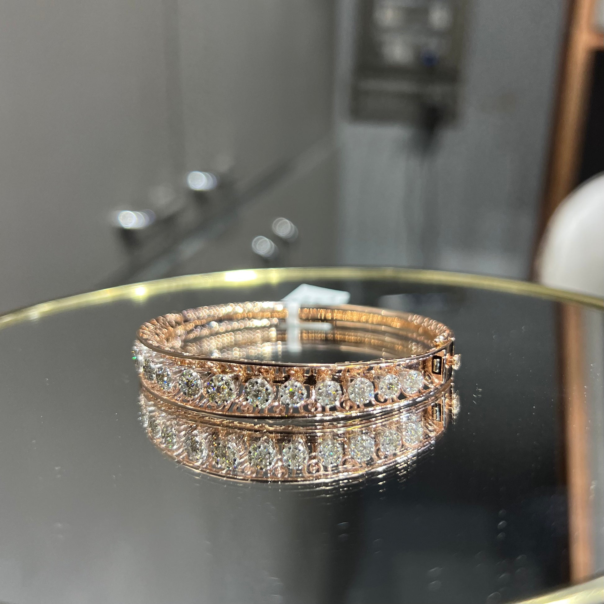 Elegant gold diamond bracelet with round-cut diamonds in a bangle design, displayed on a reflective surface.