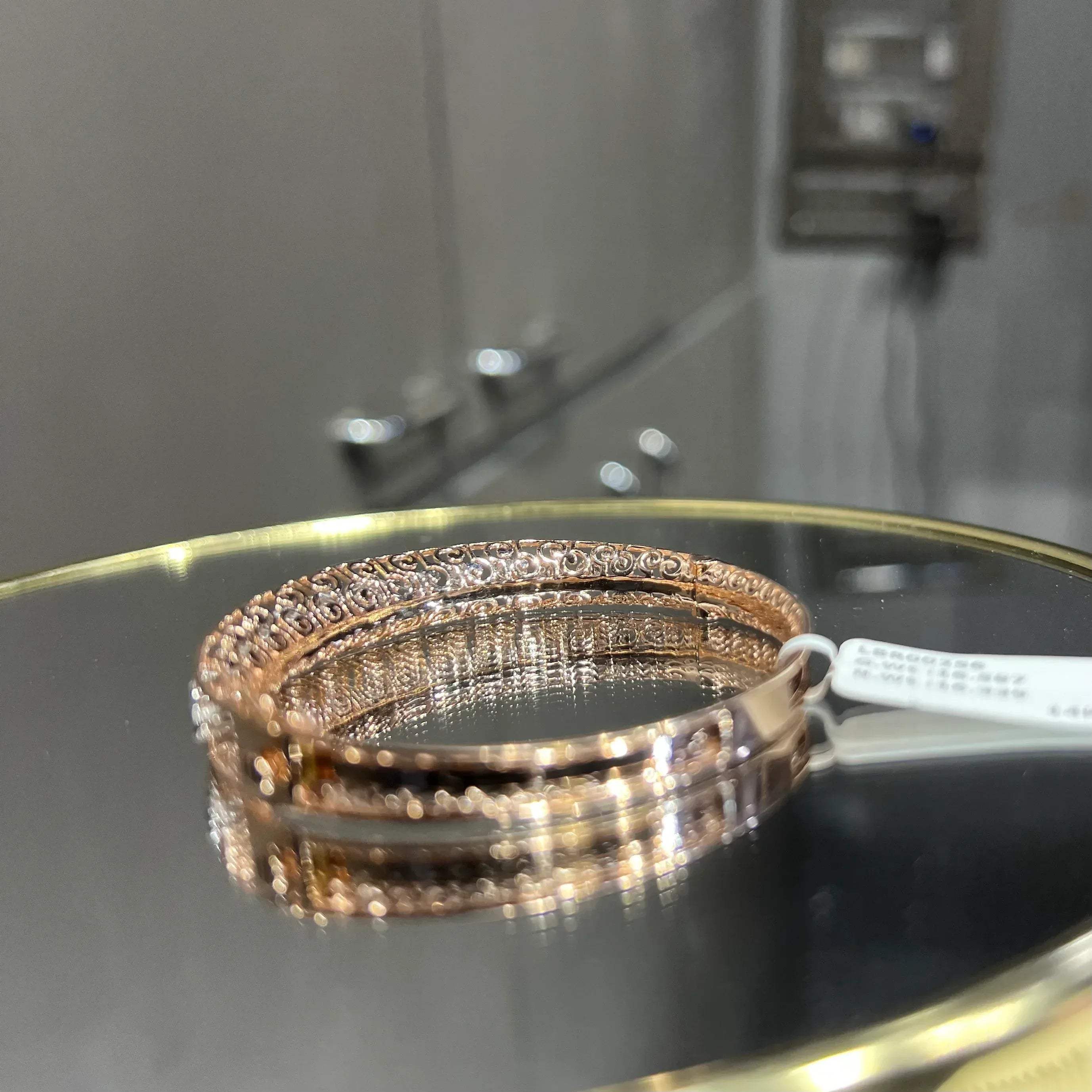 Elegant gold diamond bracelet with round-cut diamonds in a bangle design, displayed on a reflective surface.