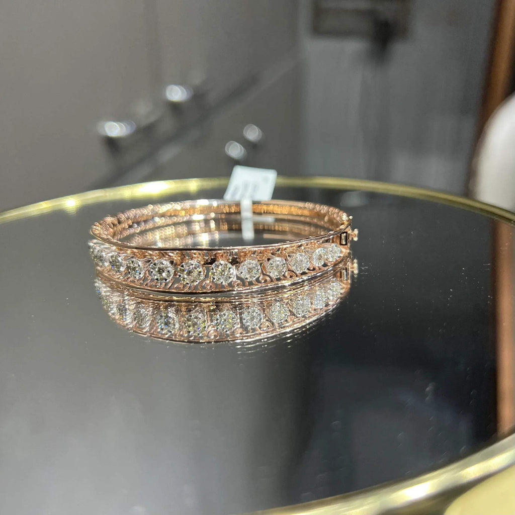 Elegant gold diamond bracelet with round-cut diamonds in a bangle design, displayed on a reflective surface.