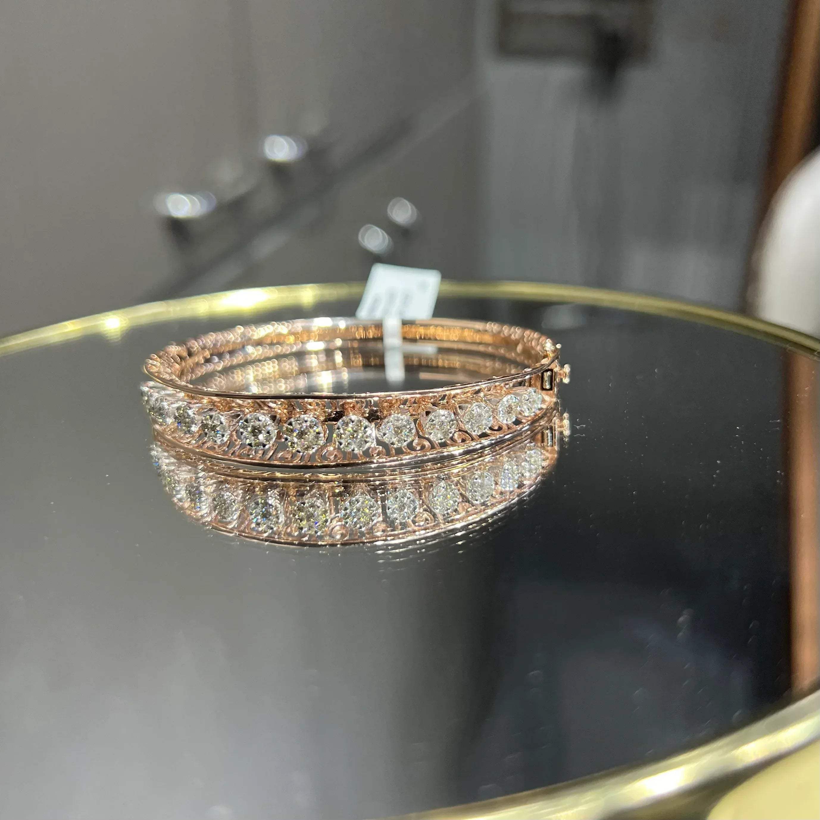 Elegant gold diamond bracelet with round-cut diamonds in a bangle design, displayed on a reflective surface.