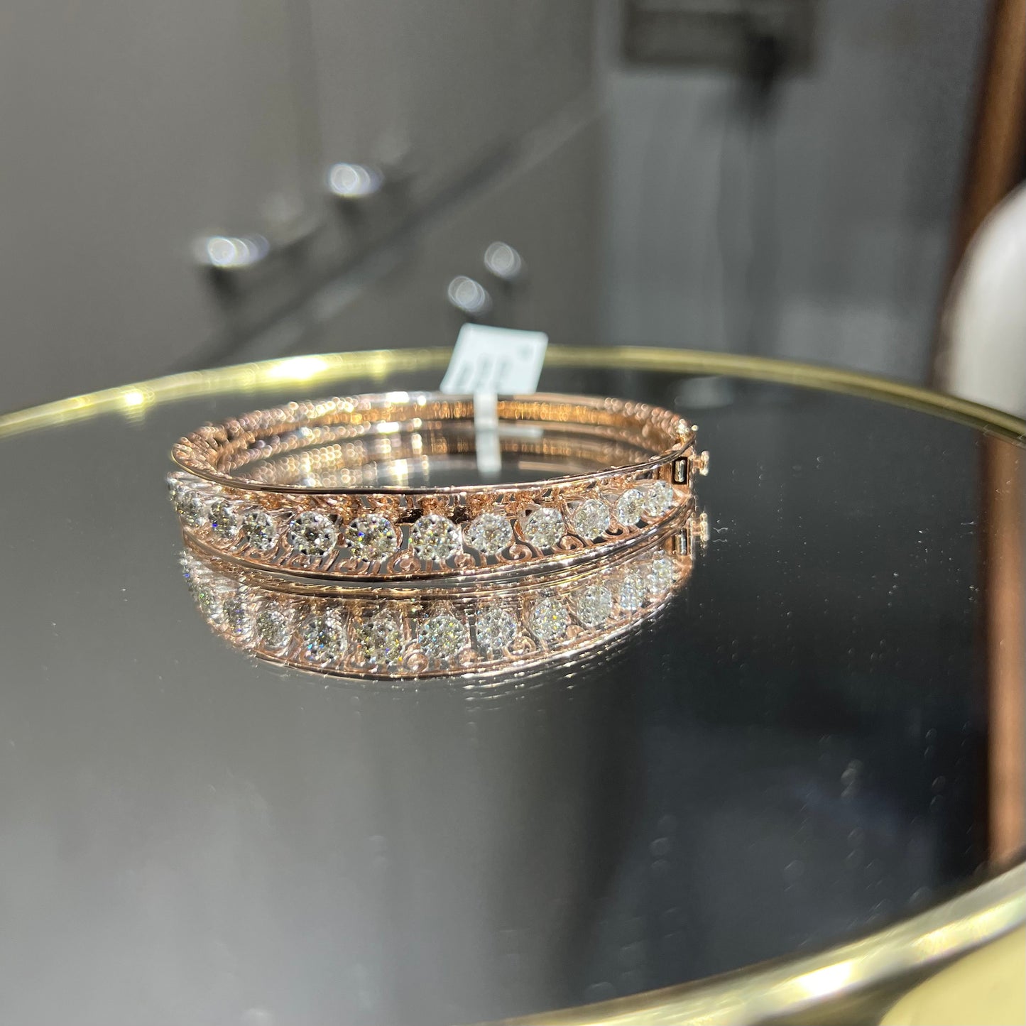 Elegant gold diamond bracelet with round-cut diamonds in a bangle design, displayed on a reflective surface.