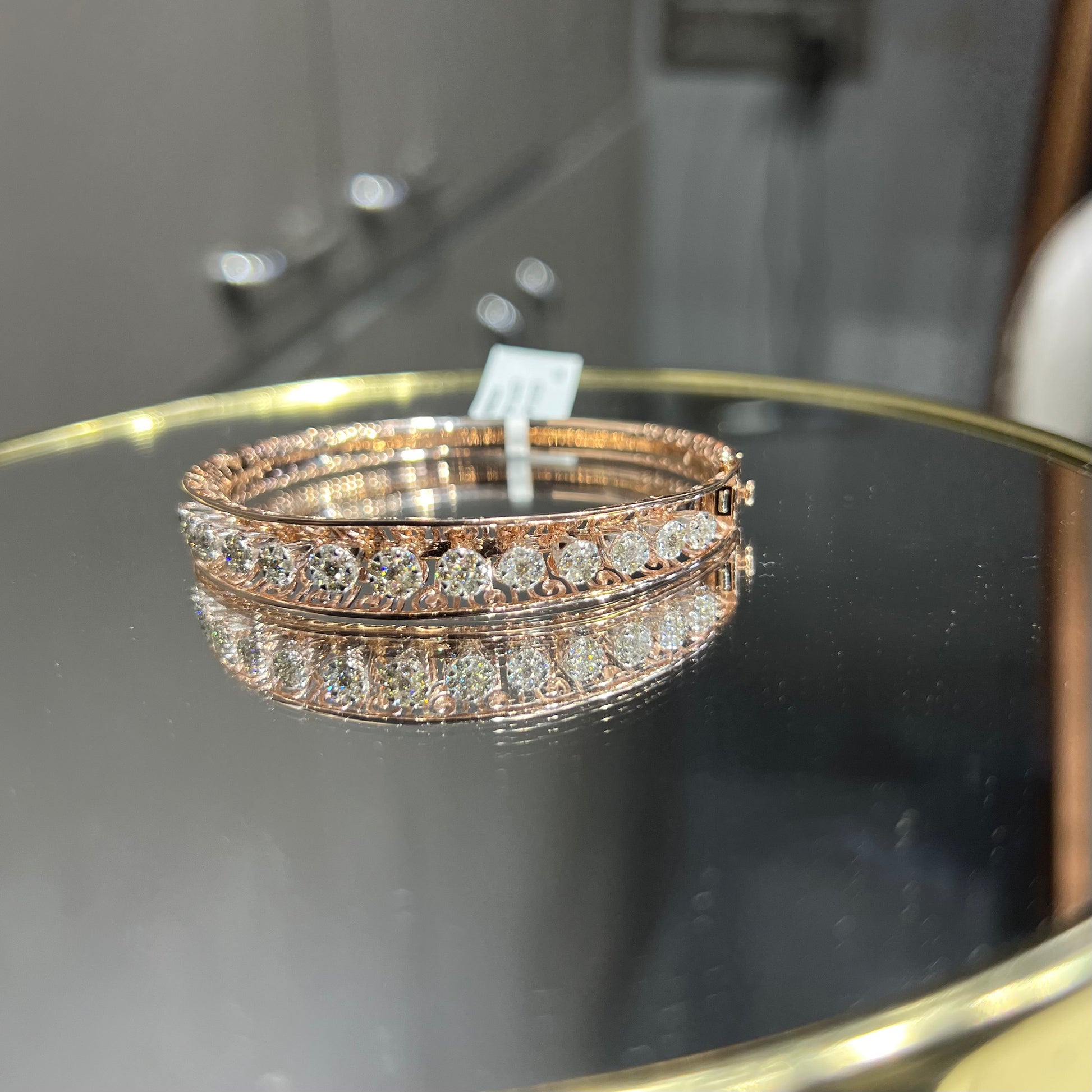 Elegant gold diamond bracelet with round-cut diamonds in a bangle design, displayed on a reflective surface.