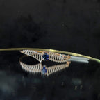A luxurious gold diamond bracelet with a brilliant cut blue stone in an openable design, displayed on a reflective surface.