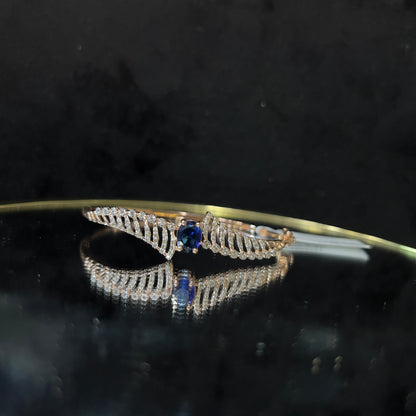 A luxurious gold diamond bracelet with a brilliant cut blue stone in an openable design, displayed on a reflective surface.