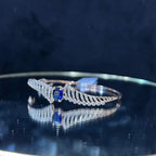 A luxurious gold diamond bracelet with a brilliant cut blue stone in an openable design, displayed on a reflective surface.