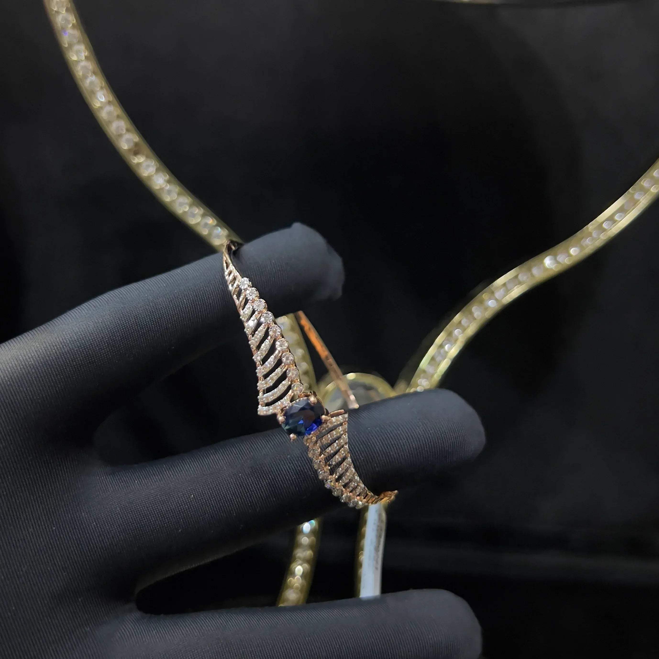 A luxurious gold diamond bracelet with a brilliant cut blue stone in an openable design, displayed by a hand.