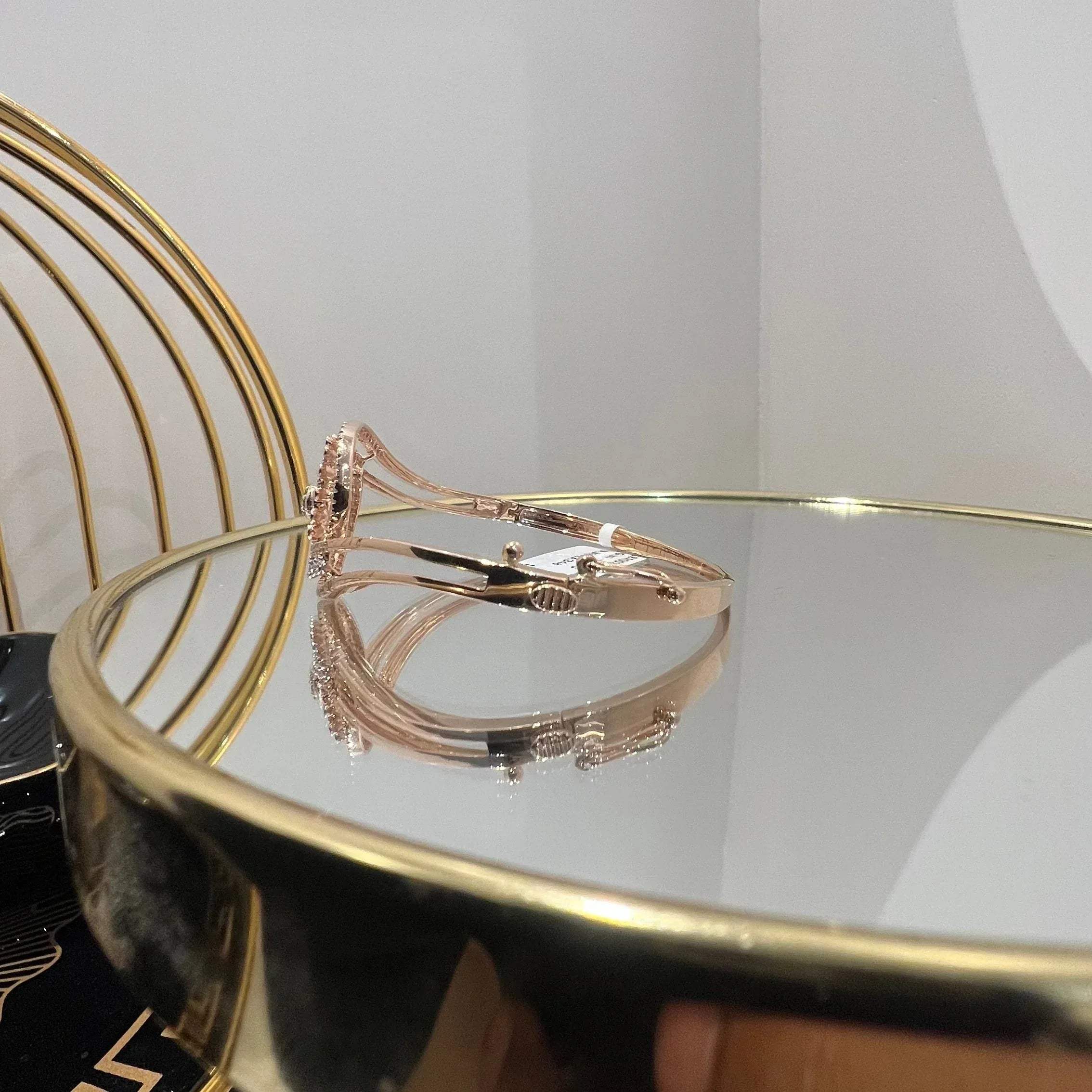 A luxurious gold diamond bracelet with a openable design, featuring a central oval-shaped diamond surrounded by smaller diamonds set in a brilliant cut, displayed on a reflective surface.