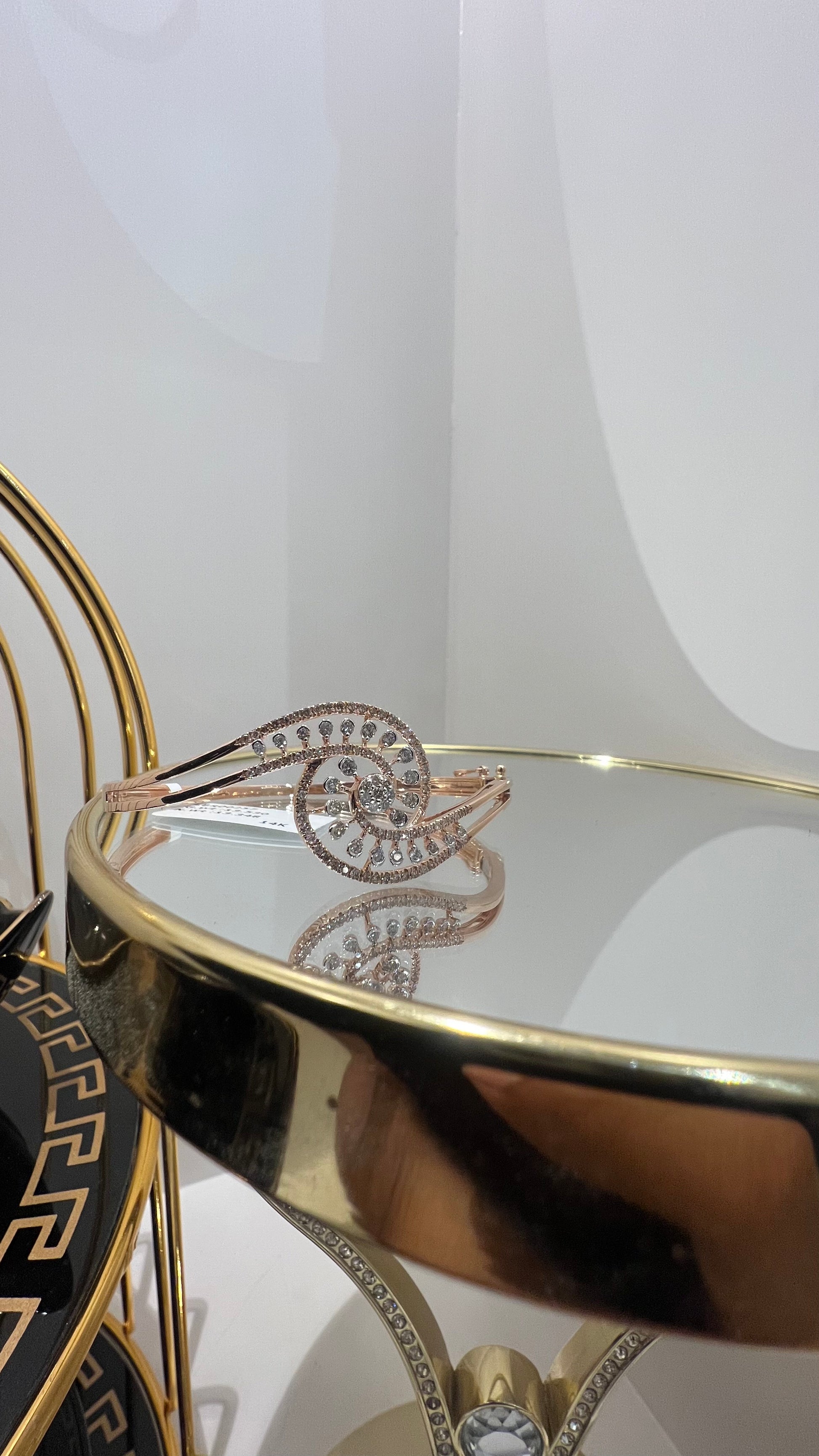 A luxurious gold diamond bracelet with a openable design, featuring a central oval-shaped diamond surrounded by smaller diamonds set in a brilliant cut, displayed on a reflective surface.