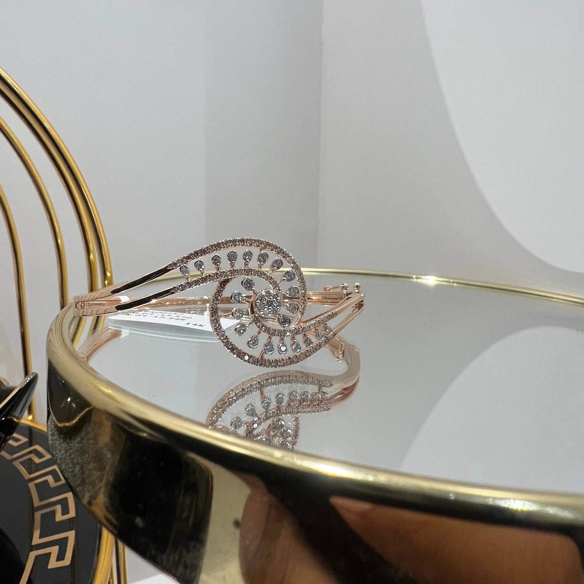 A luxurious gold diamond bracelet with a openable design, featuring a central oval-shaped diamond surrounded by smaller diamonds set in a brilliant cut, displayed on a reflective surface.