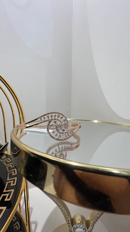 A luxurious gold diamond bracelet with a openable design, featuring a central oval-shaped diamond surrounded by smaller diamonds set in a brilliant cut, displayed on a reflective surface.