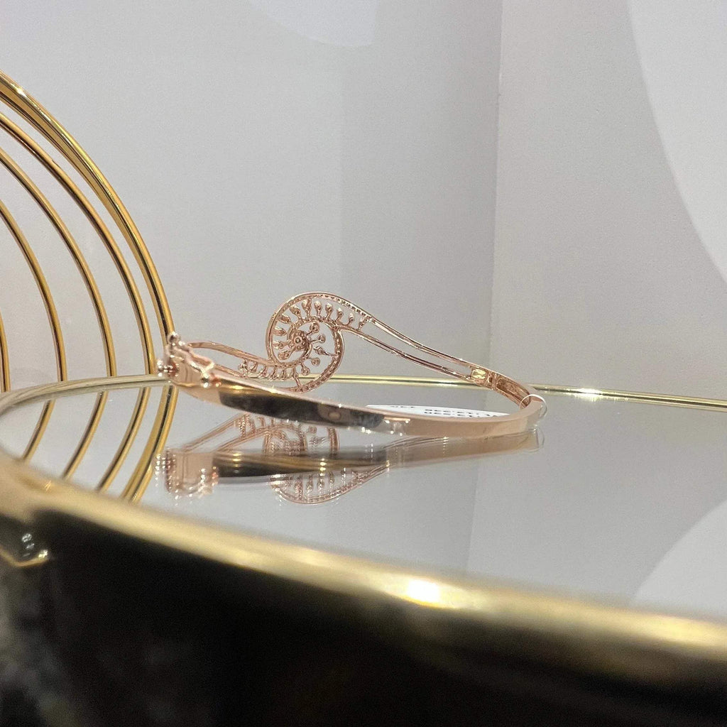 A luxurious gold diamond bracelet with a openable design, featuring a central oval-shaped diamond surrounded by smaller diamonds set in a brilliant cut, displayed on a reflective surface.