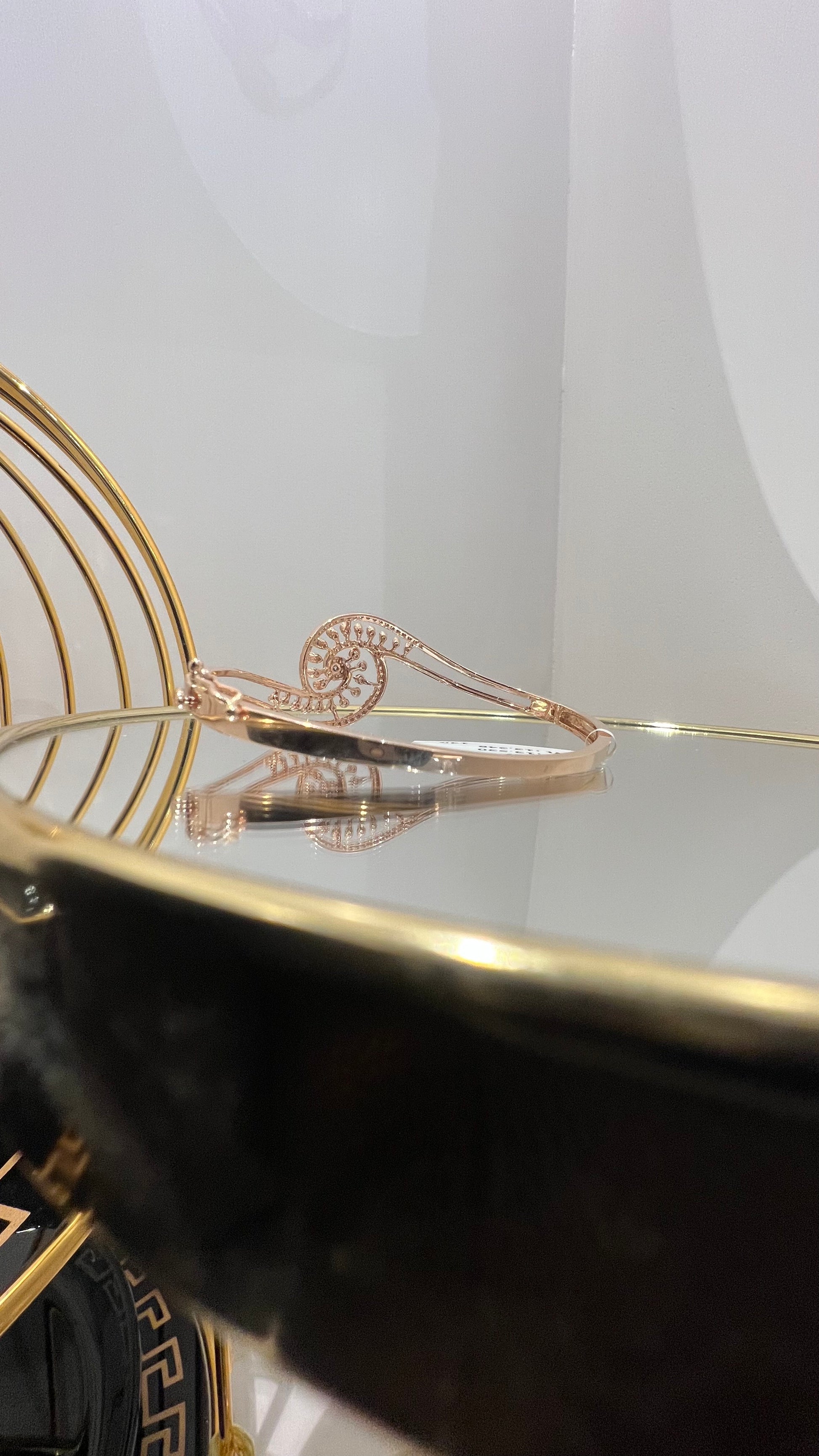 A luxurious gold diamond bracelet with a openable design, featuring a central oval-shaped diamond surrounded by smaller diamonds set in a brilliant cut, displayed on a reflective surface.