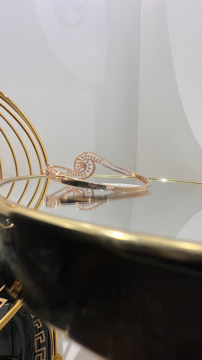 A luxurious gold diamond bracelet with a openable design, featuring a central oval-shaped diamond surrounded by smaller diamonds set in a brilliant cut, displayed on a reflective surface.