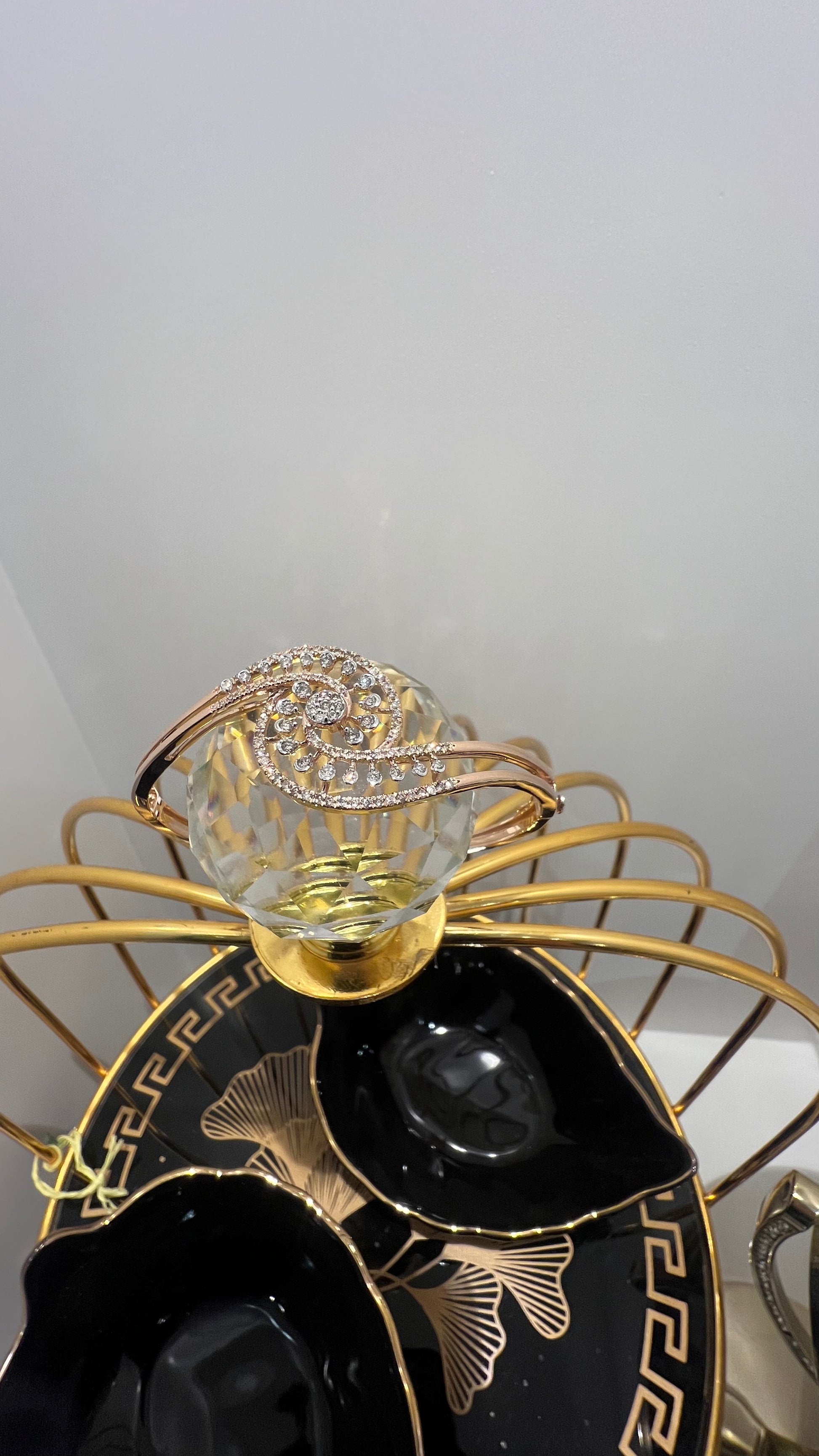 A luxurious gold diamond bracelet with a openable design, featuring a central oval-shaped diamond surrounded by smaller diamonds set in a brilliant cut, displayed on a glass ball.