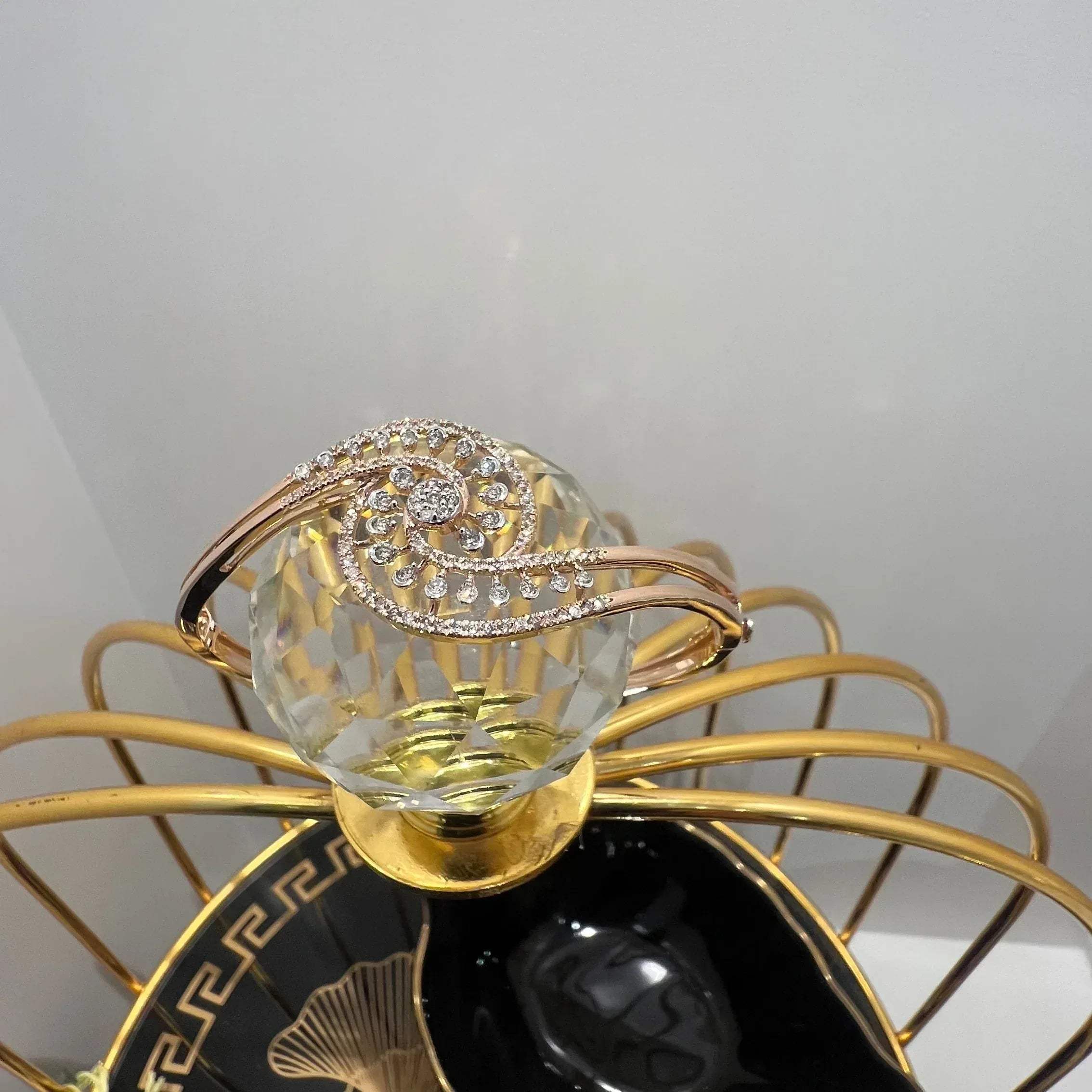 A luxurious gold diamond bracelet with a openable design, featuring a central oval-shaped diamond surrounded by smaller diamonds set in a brilliant cut, displayed on a glass ball.