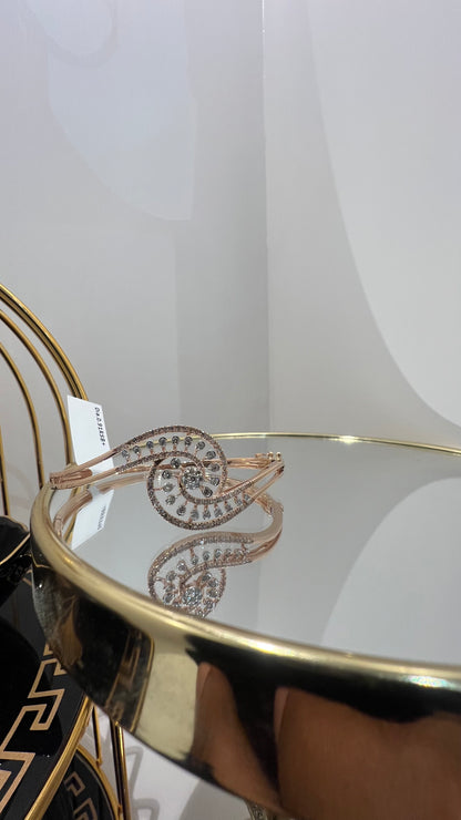 A luxurious gold diamond bracelet with a openable design, featuring a central oval-shaped diamond surrounded by smaller diamonds set in a brilliant cut, displayed on a reflective surface.