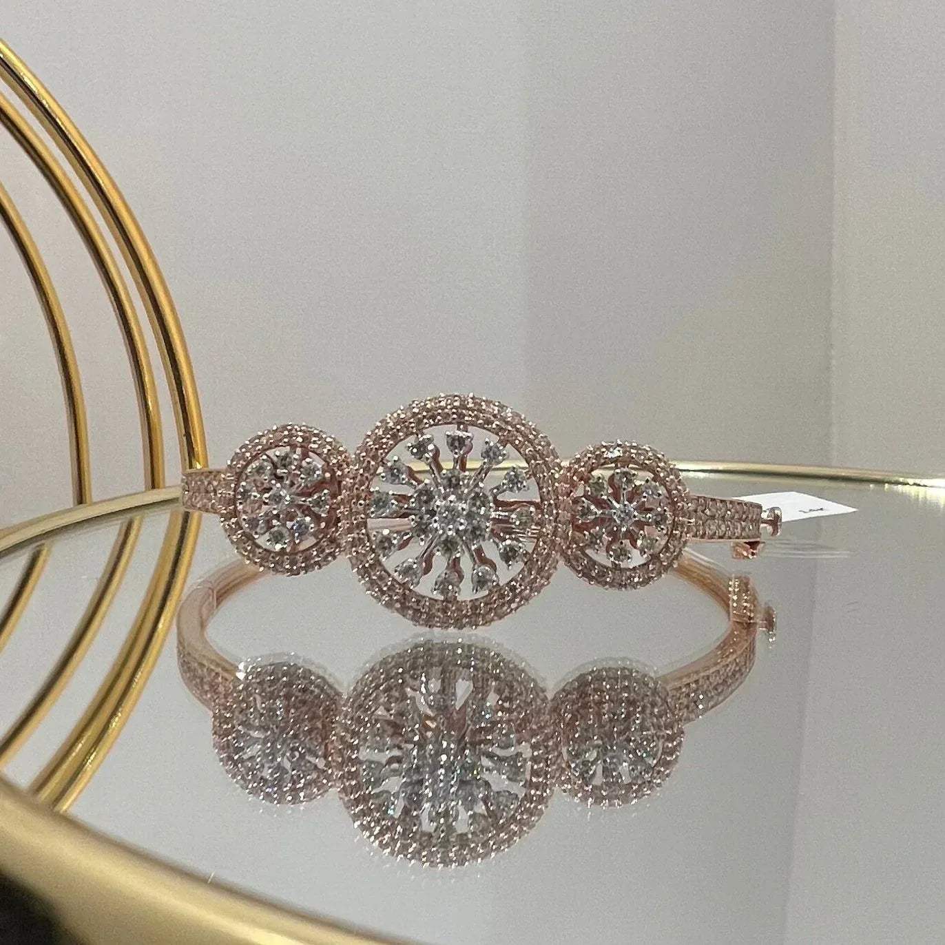 A gold diamond bracelet with a central oval-shaped diamond surrounded by smaller diamonds, displayed on a reflective surface.