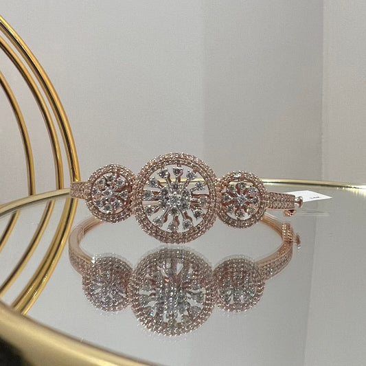 A gold diamond bracelet with a central oval-shaped diamond surrounded by smaller diamonds, displayed on a reflective surface.