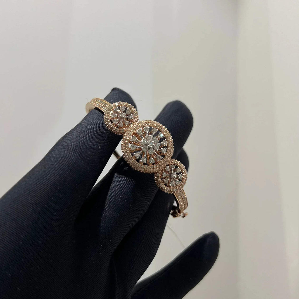 A gold diamond bracelet with a central oval-shaped diamond surrounded by smaller diamonds, displayed by a hand.