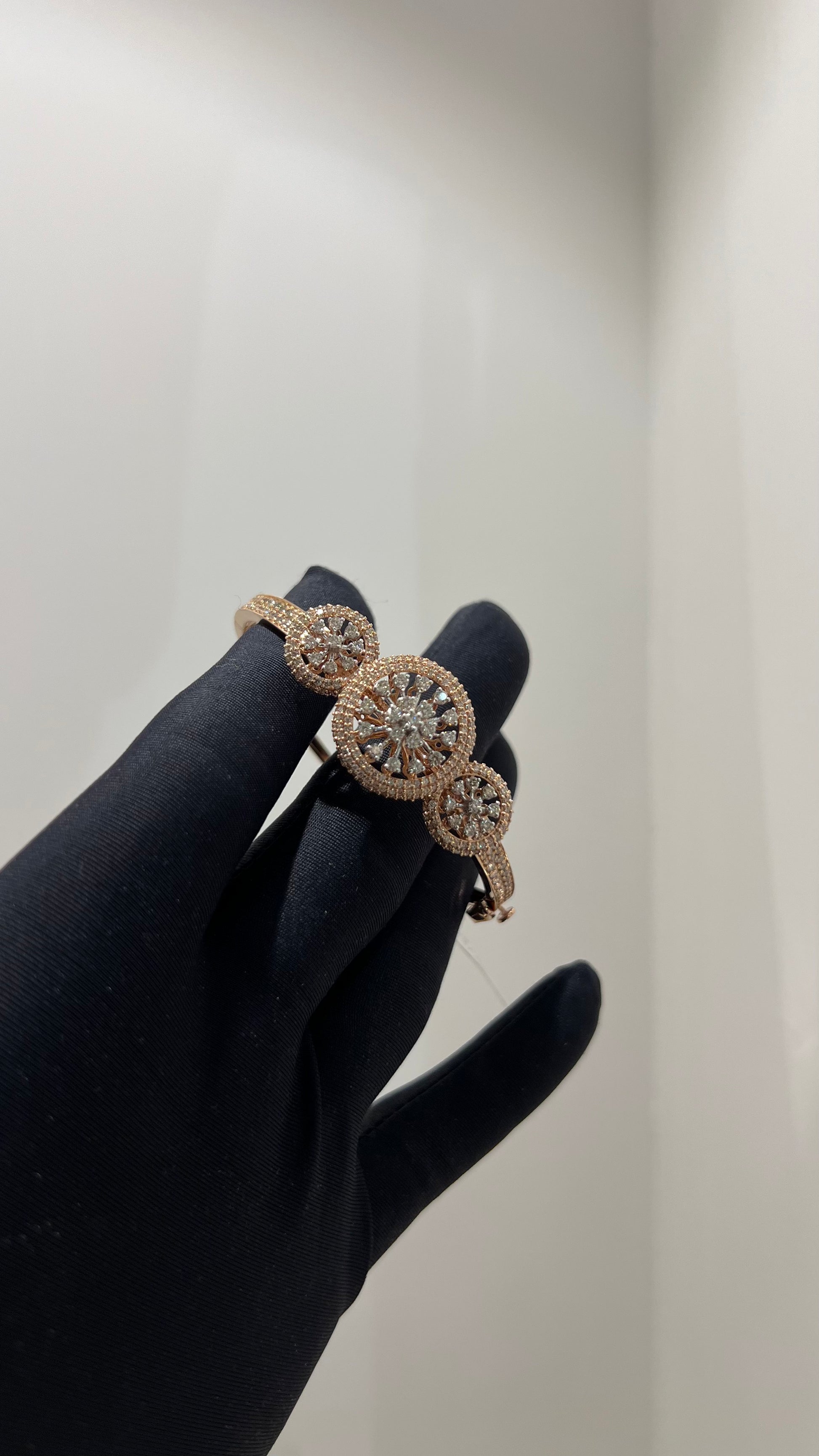 A gold diamond bracelet with a central oval-shaped diamond surrounded by smaller diamonds, displayed by a hand.