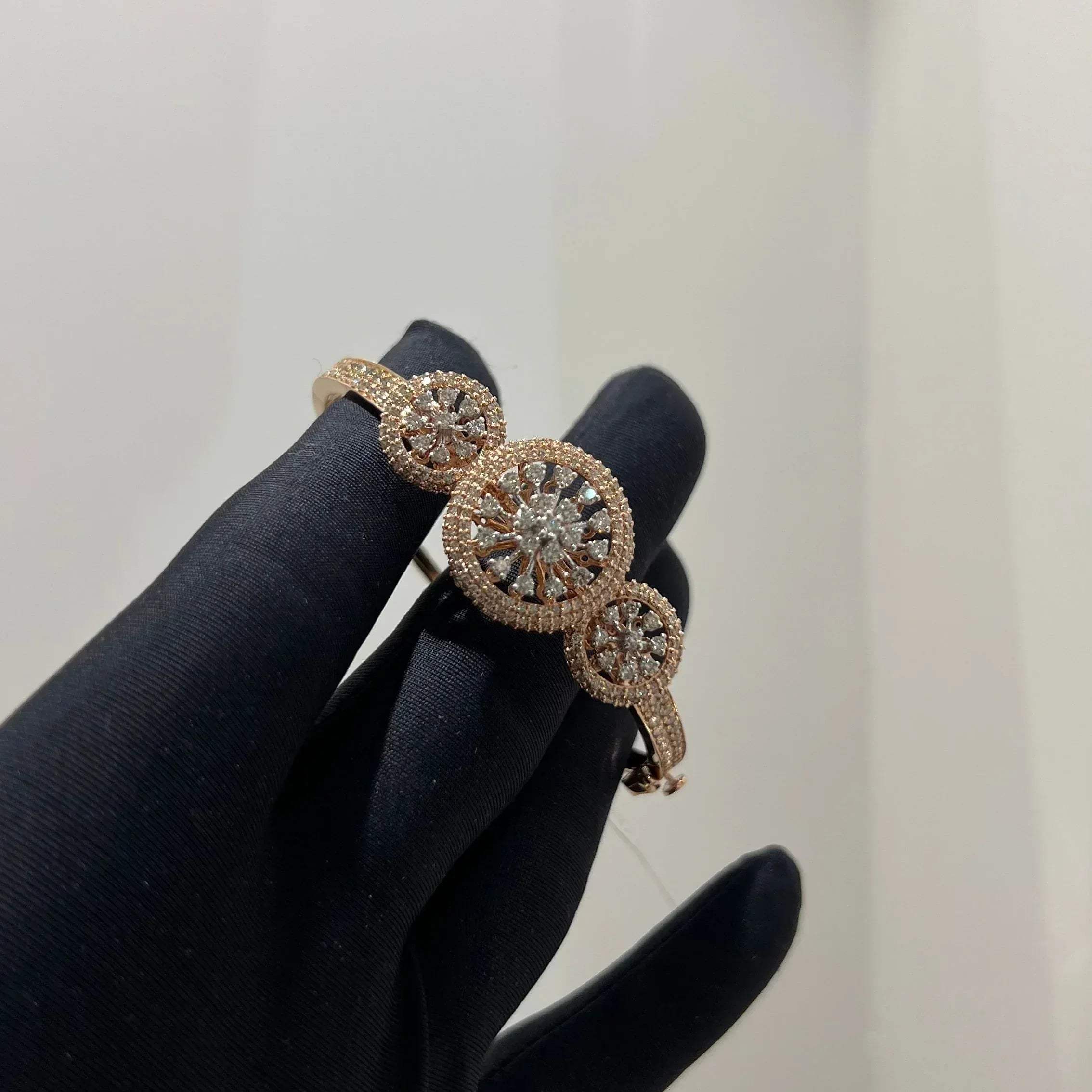 A gold diamond bracelet with a central oval-shaped diamond surrounded by smaller diamonds, displayed by a hand.
