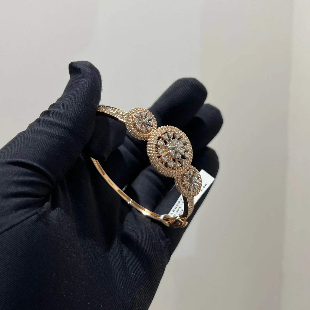A gold diamond bracelet with a central oval-shaped diamond surrounded by smaller diamonds, displayed by a hand.