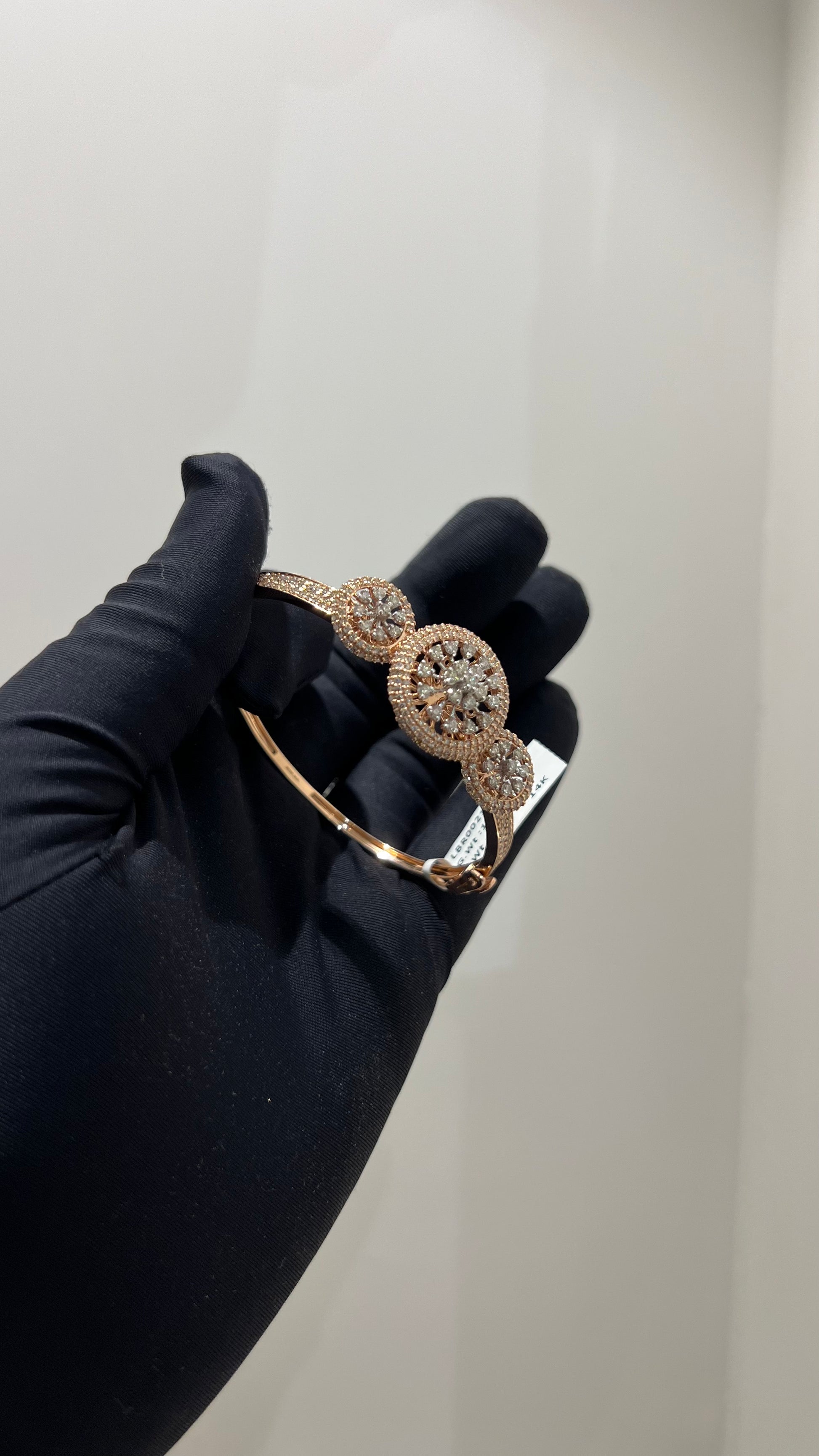 A gold diamond bracelet with a central oval-shaped diamond surrounded by smaller diamonds, displayed by a hand.