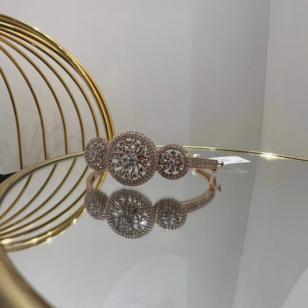 A gold diamond bracelet with a central oval-shaped diamond surrounded by smaller diamonds, displayed on a reflective surface.