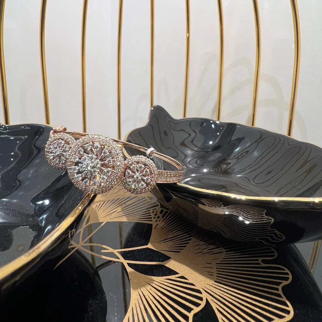 A gold diamond bracelet with a central oval-shaped diamond surrounded by smaller diamonds, displayed on a black surface.