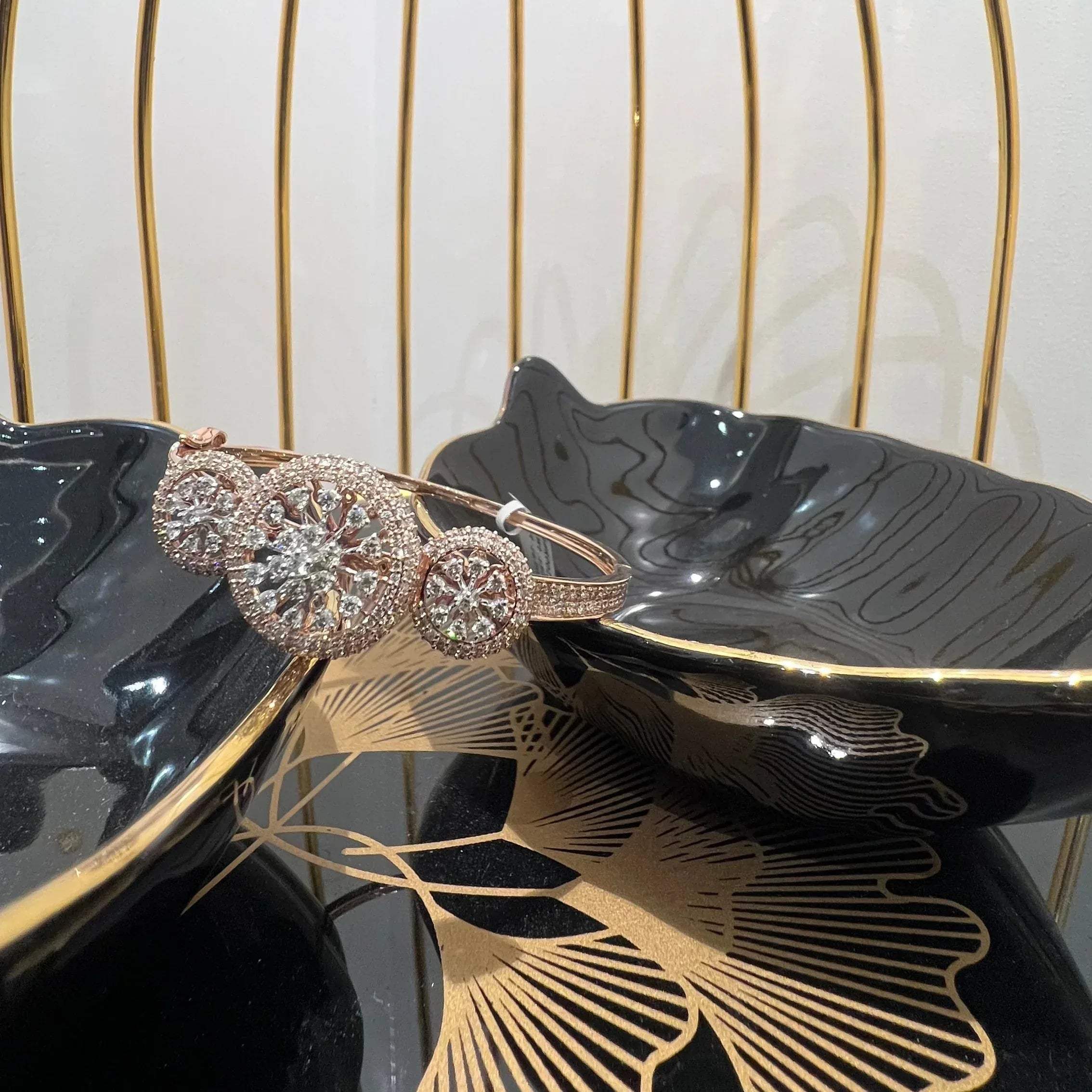 A gold diamond bracelet with a central oval-shaped diamond surrounded by smaller diamonds, displayed on a black surface.