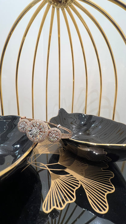 A gold diamond bracelet with a central oval-shaped diamond surrounded by smaller diamonds, displayed on a black surface.