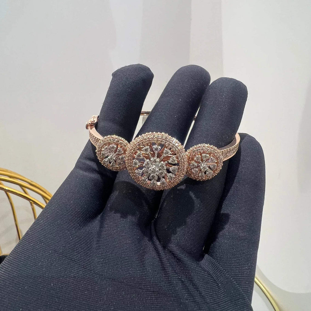 A gold diamond bracelet with a central oval-shaped diamond surrounded by smaller diamonds, displayed by a hand.