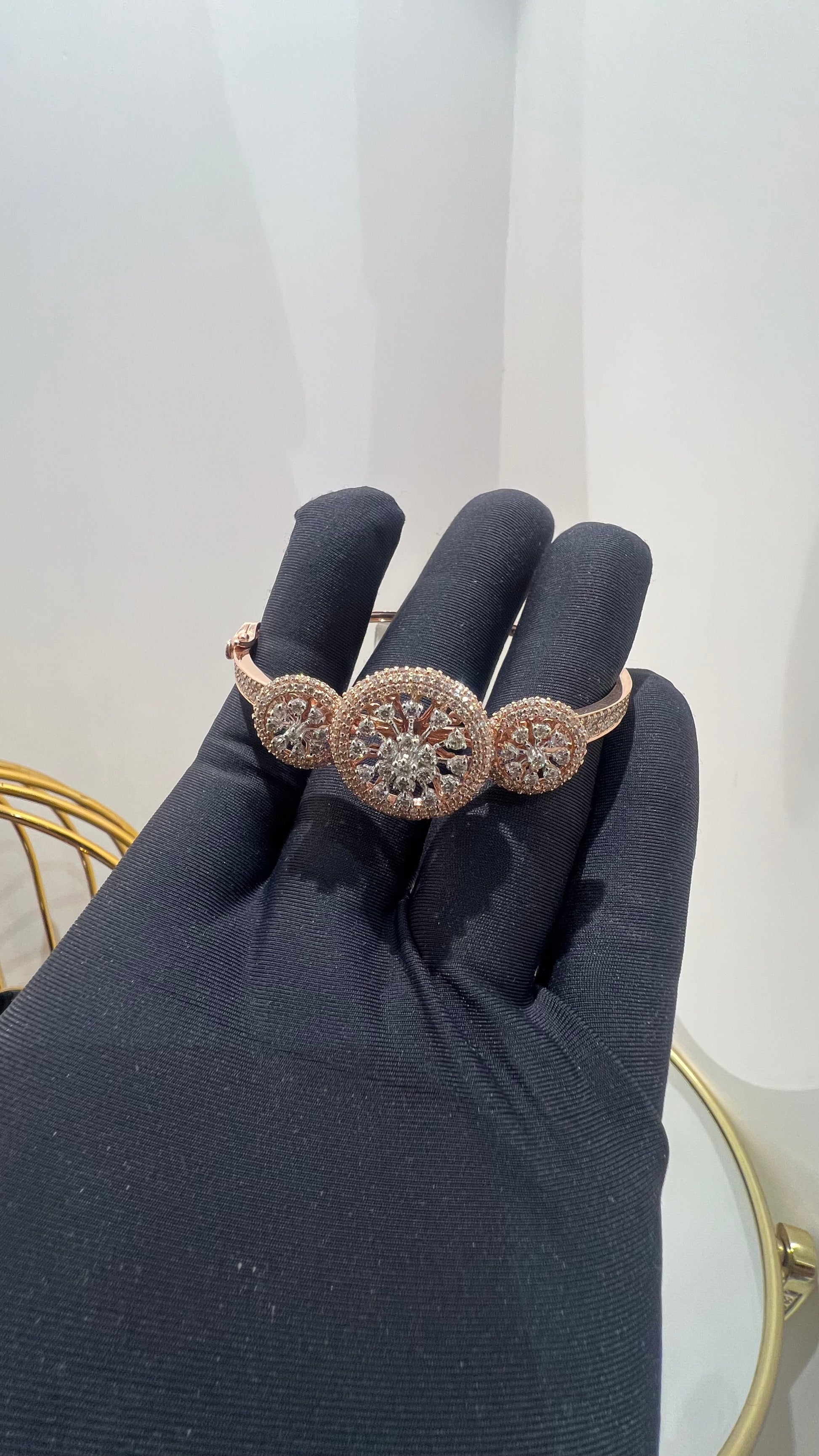 A gold diamond bracelet with a central oval-shaped diamond surrounded by smaller diamonds, displayed by a hand.