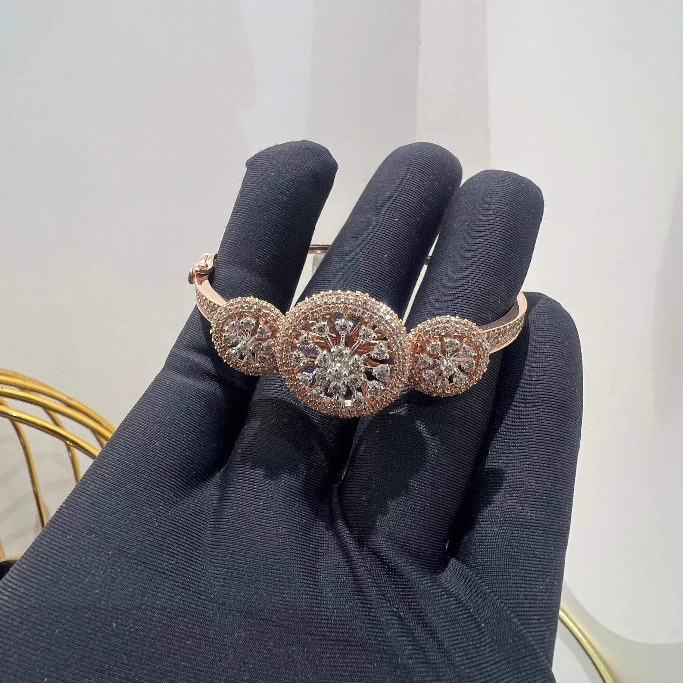 A gold diamond bracelet with a central oval-shaped diamond surrounded by smaller diamonds, displayed by a hand.