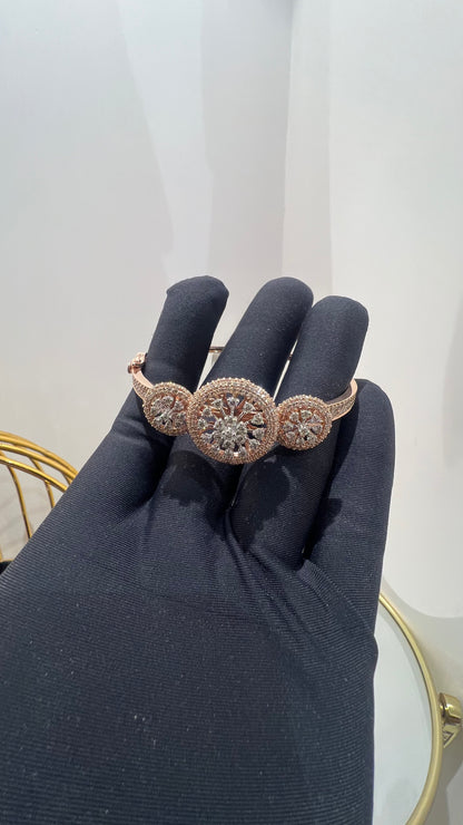 A gold diamond bracelet with a central oval-shaped diamond surrounded by smaller diamonds, displayed by a hand.