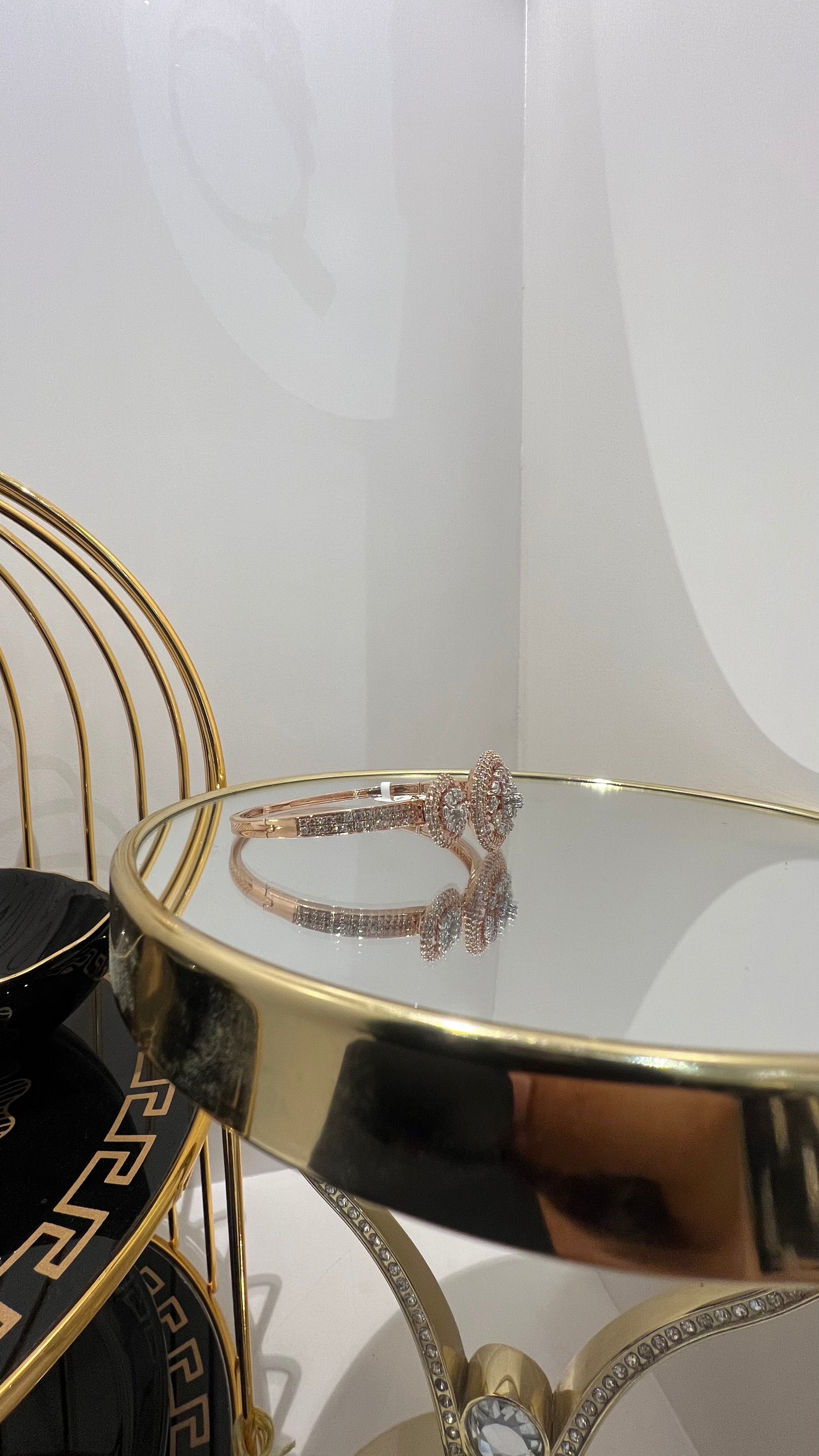 A gold diamond bracelet with a central oval-shaped diamond surrounded by smaller diamonds, displayed on a reflective surface.