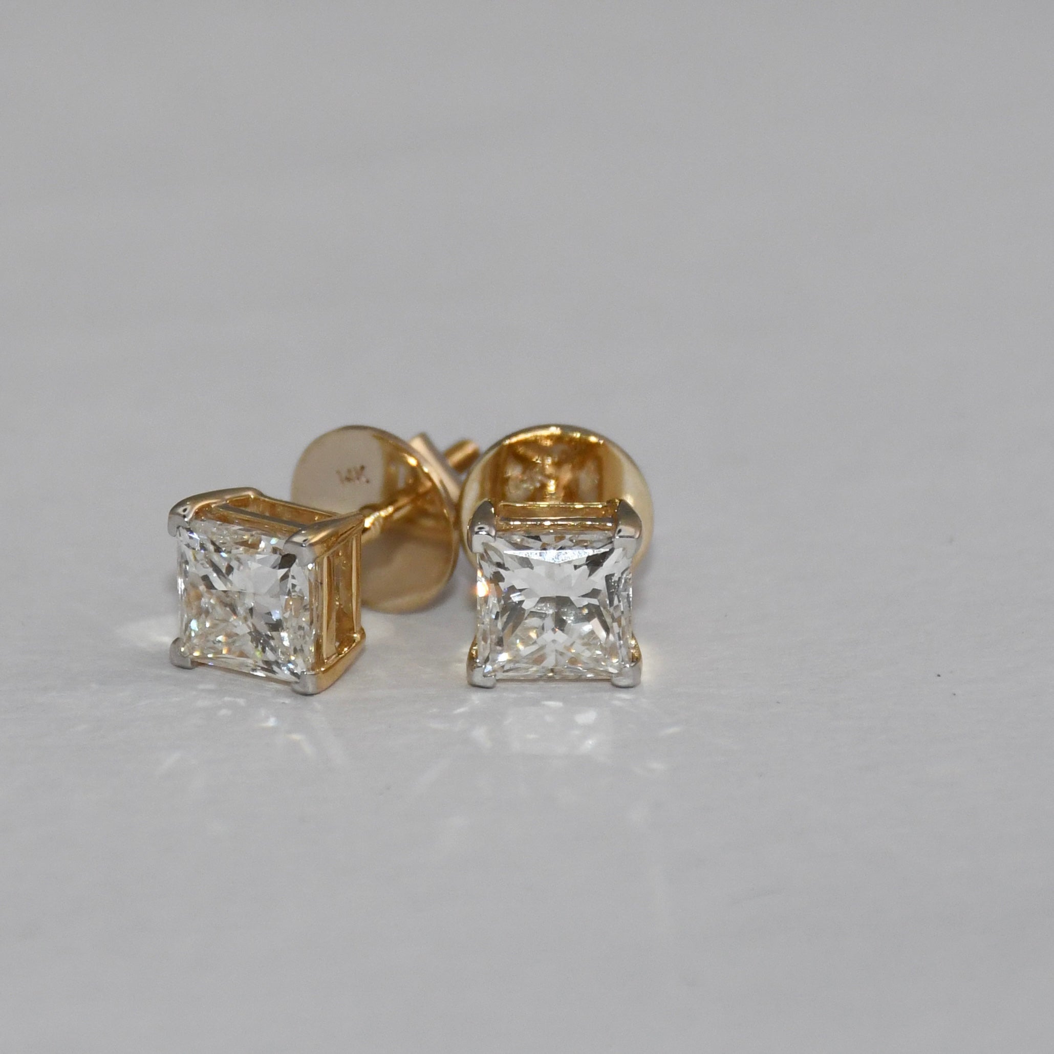 Gold princess-cut diamond earrings on a gray background