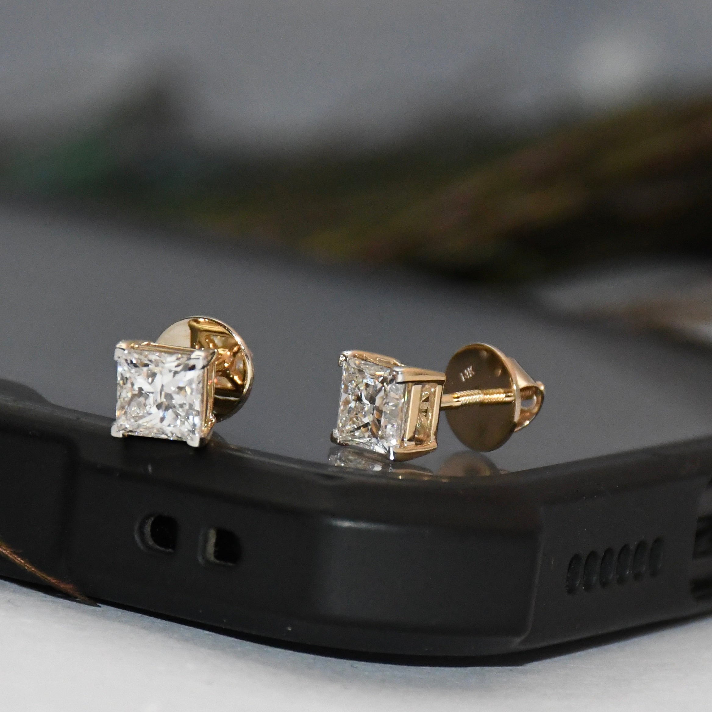 Gold diamond stud earrings on a black phone case with a blurred background