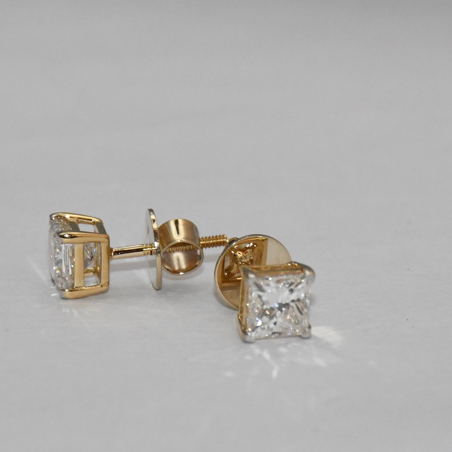 Gold princess-cut diamond earrings on a light gray background