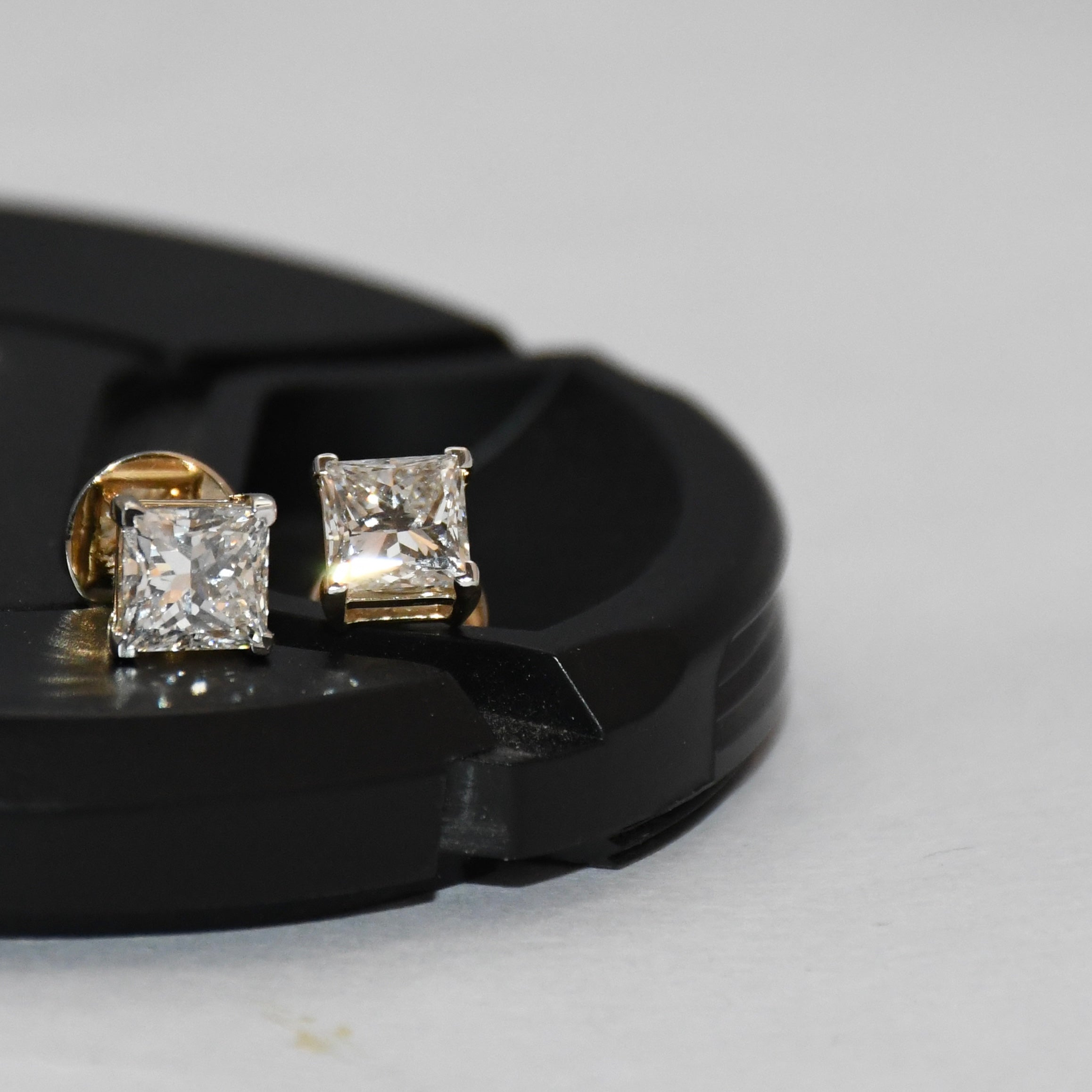 Gold earrings with princess-cut diamonds on a black stand against a light gray background
