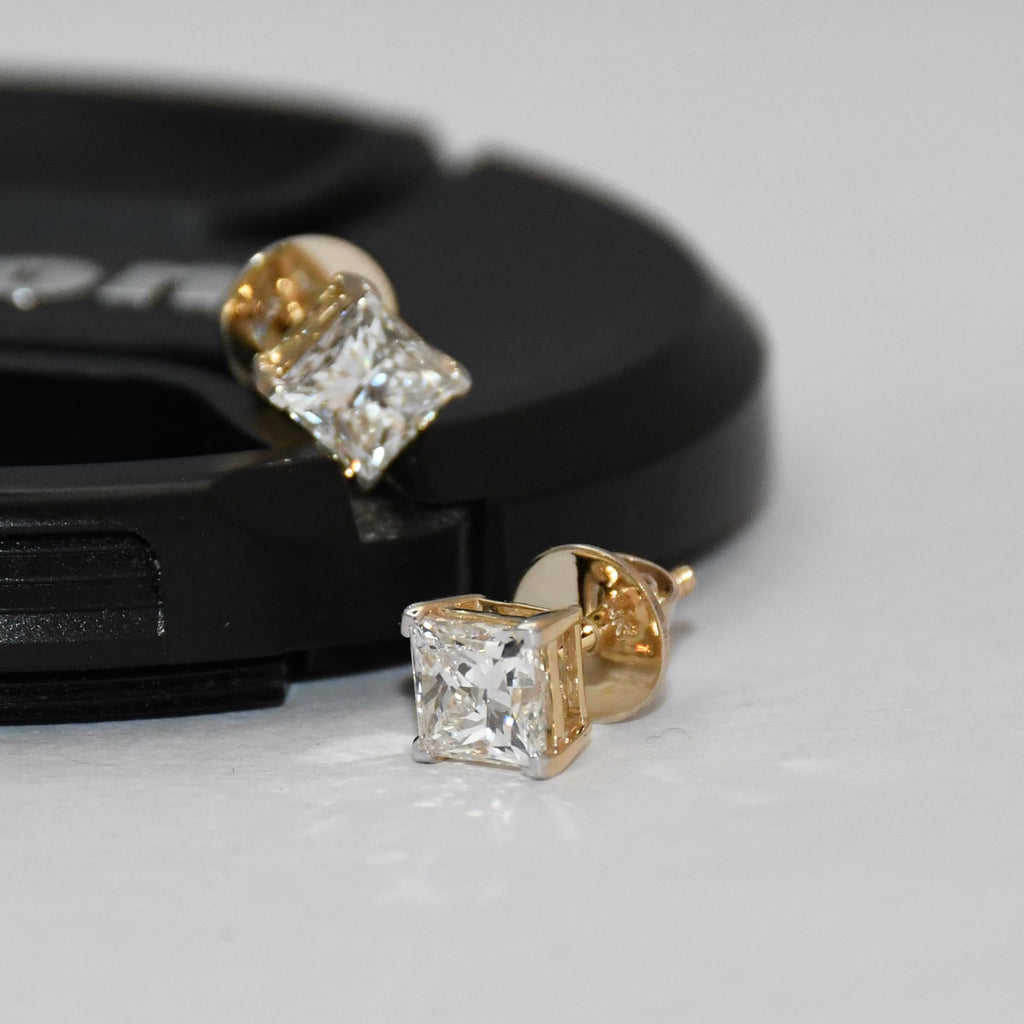 Gold diamond stud earrings on a gray surface with a black background