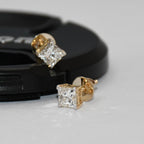 Gold diamond stud earrings on a gray surface with a black background