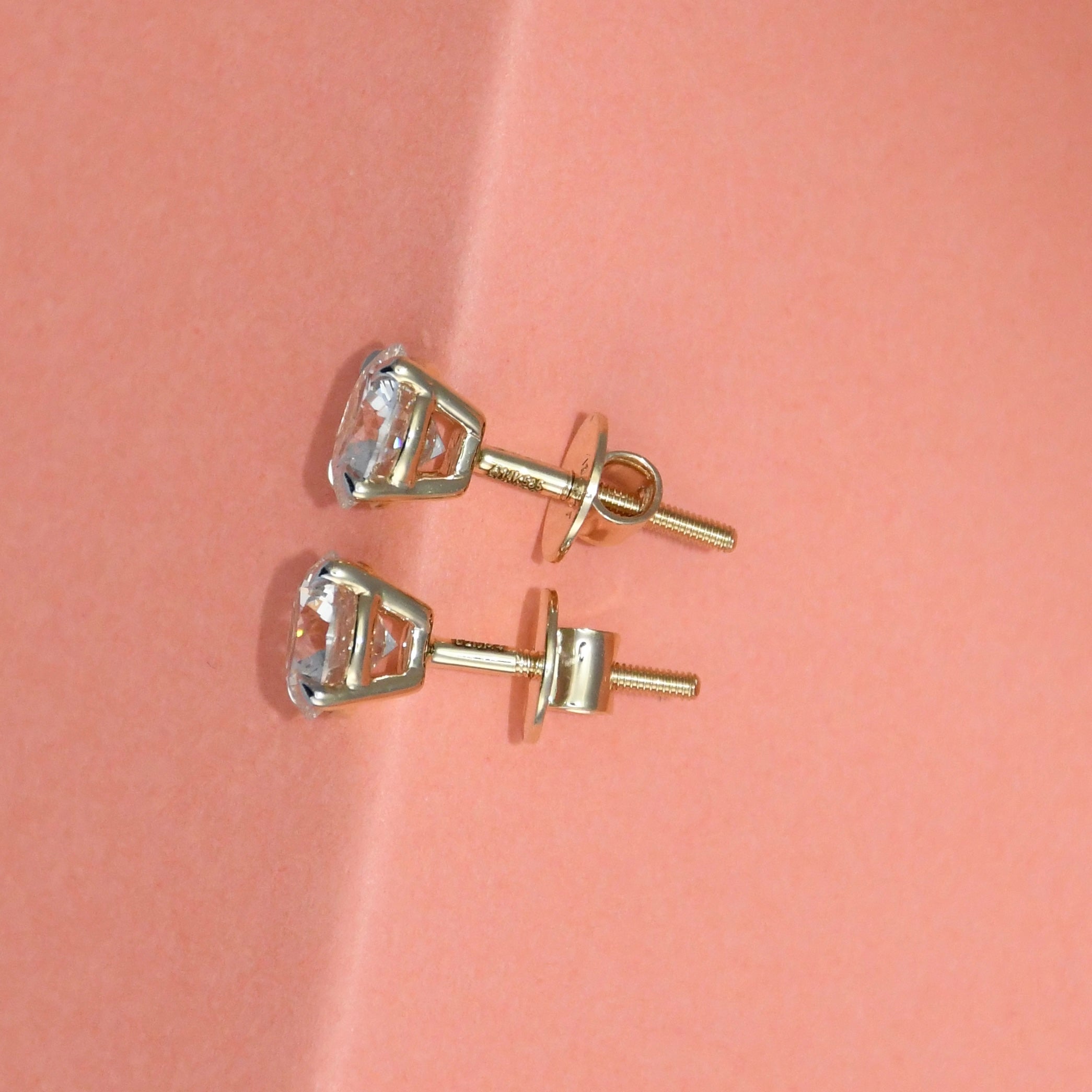 Gold stud earrings with clear diamonds on a pink background