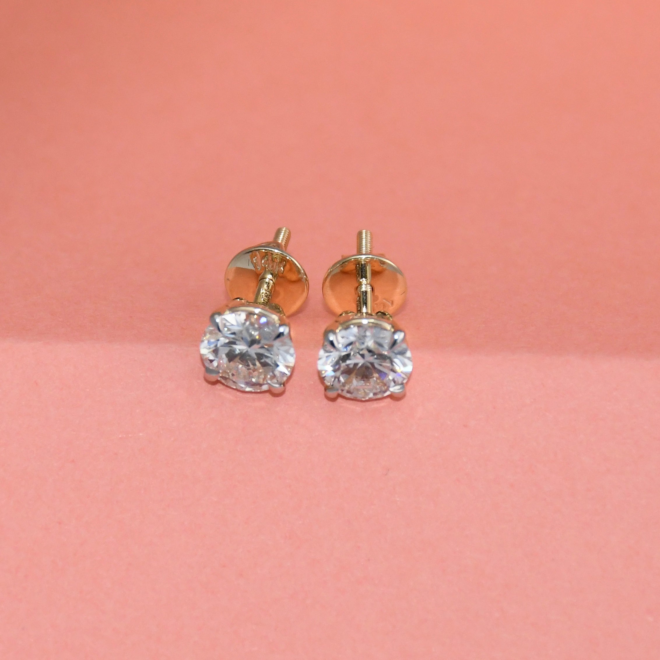 Gold stud earrings with clear diamonds on a pink background