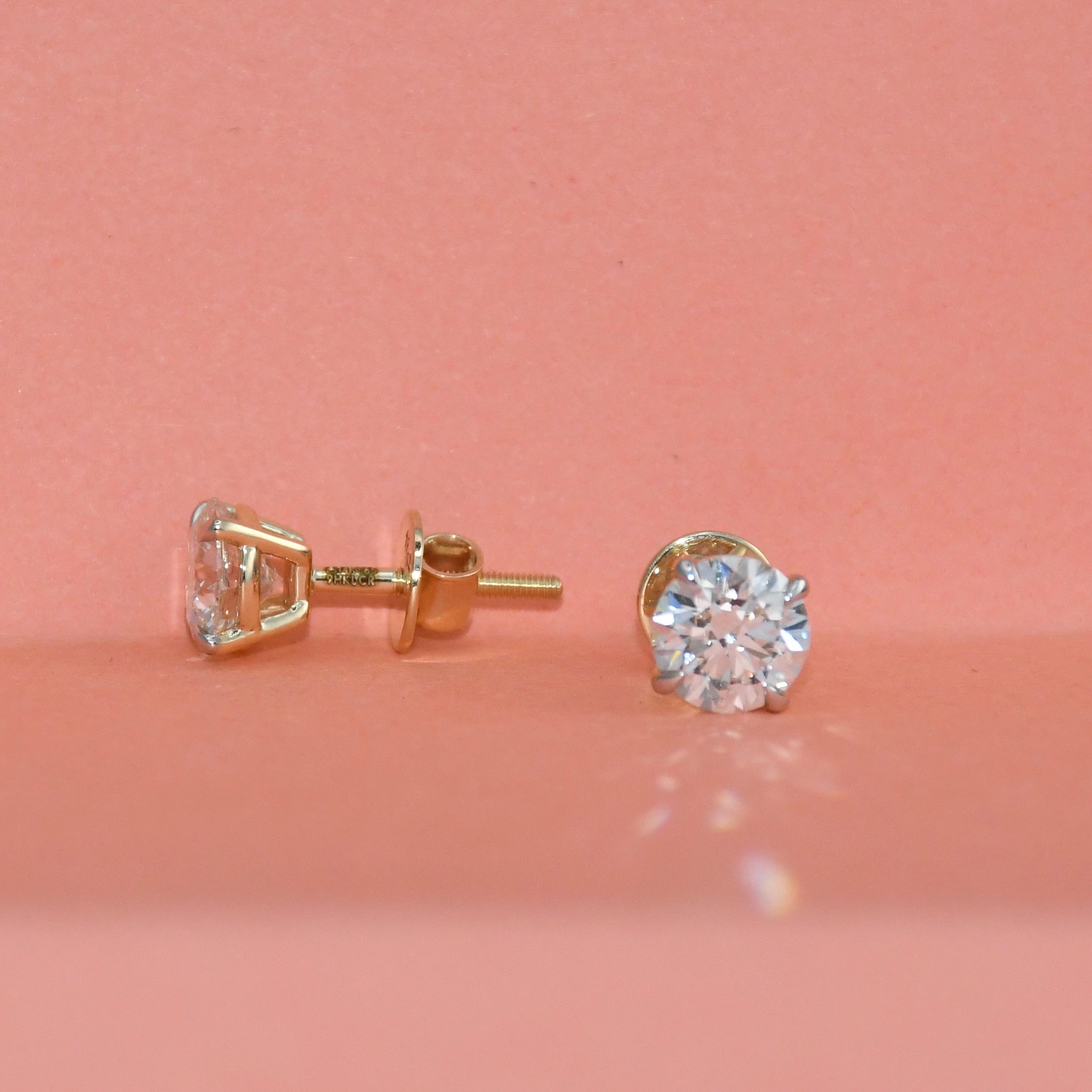 Gold diamond stud earrings on a pink background