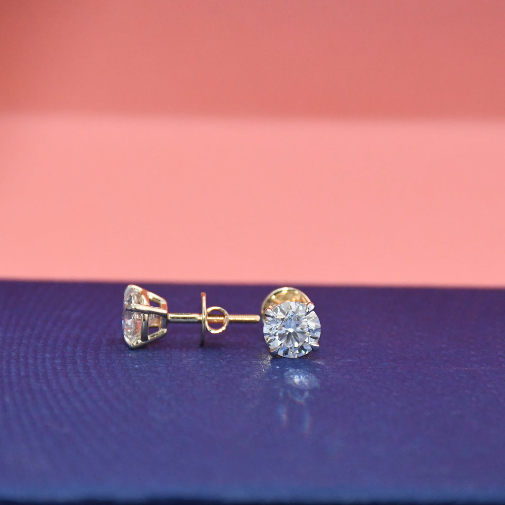Gold diamond stud earrings on a pink and blue gradient background