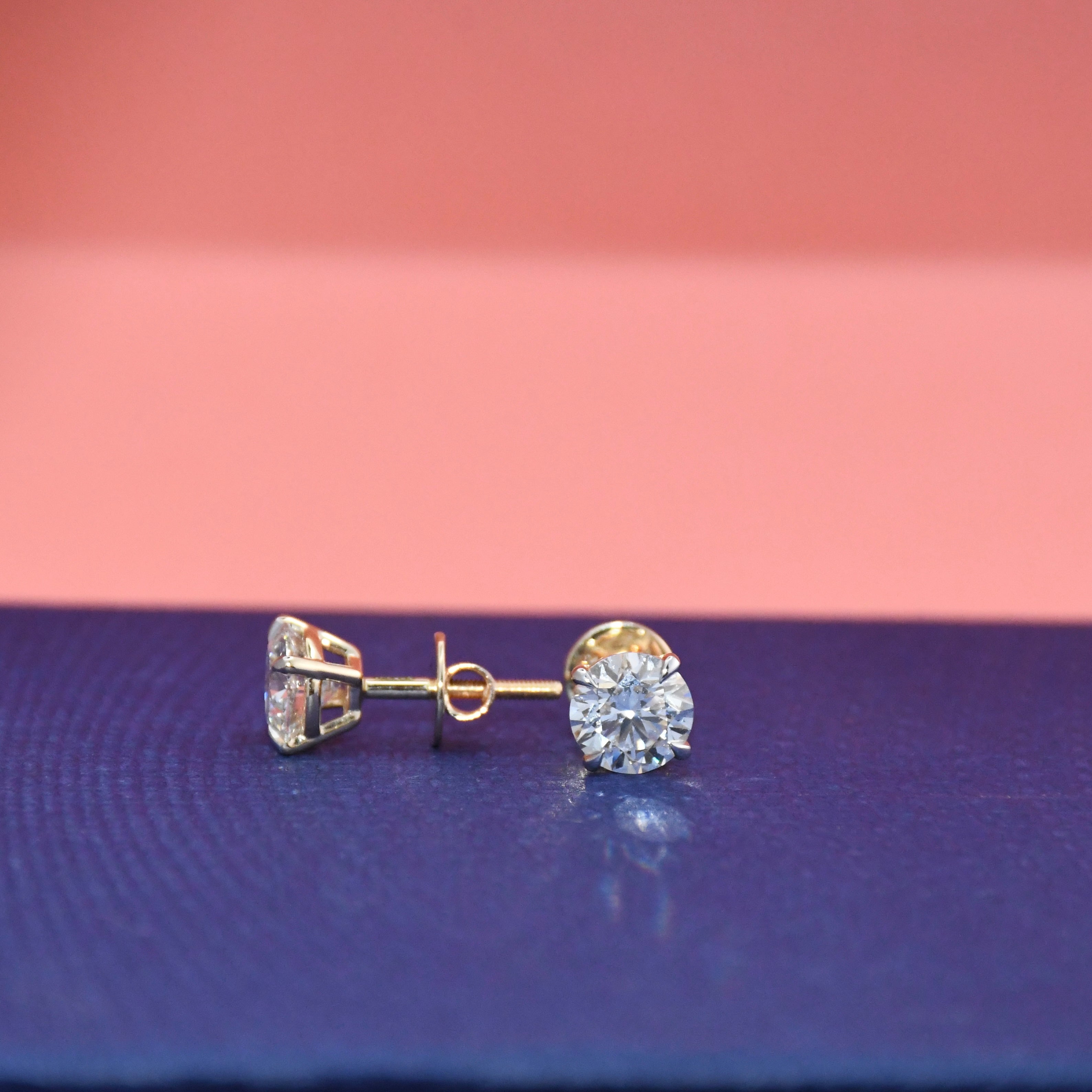 Gold diamond stud earrings on a pink and blue gradient background